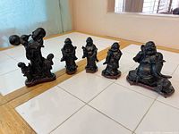 All five resin Laughing Buddha figurines on tiled surface