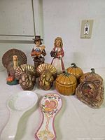 group shot showing all Thanksgiving themed figurines, pumpkins, plaque and spoon rests