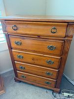 Front view of five-drawer solid wood dresser showing honey finish, brass-tone pulls, carved details