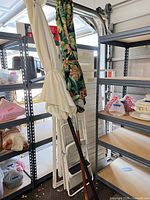 Two folded patio umbrellas, cream and tropical floral, with wood and metal poles leaning against shelving
