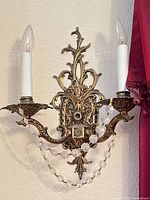 Ornate two-arm brass wall sconce with candle sleeves and crystal bead garland