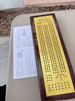 Top view of wood-framed cribbage board and instruction sheet