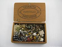 Wooden cigar box open, showing assorted earrings piled inside