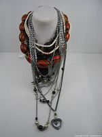 Multiple necklaces on bust: red-orange bead collar, white bead strand, several silver-tone chain necklaces with beads and heart pendant