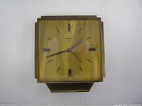 Front view of square Birks 8 brass-tone travel alarm clock showing dial, hands, hour markers