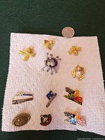 Front view of all twelve lapel pins and brooches displayed on white cloth with quarter for scale