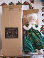 Box labeled Avon Fine Collectibles beside doll in green dress on stand