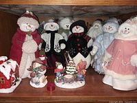 Shelf view showing multiple plush snowmen and ceramic figurines