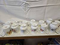 Thirteen mugs upside-down showing floral designs and ribbed forms