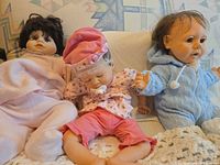 Three baby dolls seated side by side showing outfits and sizes