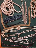 All necklaces arranged on green surface showing variety of pearl, bead and chain styles and colors