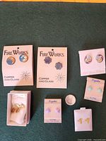 Front view showing all seven earring pairs on cards or in boxes with coin for scale