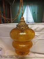 Full view of amber glass pendant light with chain and ornate cap
