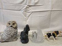 Front view of four items: owl, dark stone animal, cat candle holder, cow