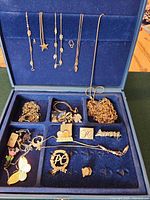 Open blue Avon jewelry case showing assorted necklaces on lid hooks and mixed jewelry pieces in compartments