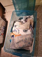 Clear plastic tub containing mixed fabric remnants, sewing pattern envelopes and lace trim