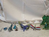 Group shot of six small glass and metal figurines including fish, bird, triangular figure, butterfly, dragonfly and green owl