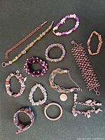 All 14 bracelets laid out showing variety of materials, colors and styles with coin for scale