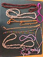 Overview of all seven necklaces arranged on black surface showing colours, bead types and styles