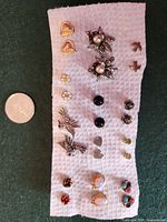 Front view of all stud earring pairs arranged on paper towel with coin for scale
