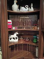 Corner bookcase shelves showing books, figurines, brass scale and other decor