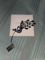 Front view of peacock brooch on display card showing multicolor rhinestones and lavender stone body
