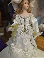 Full view of doll standing showing gown, hat, ribbons