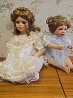 Front view of both dolls seated, showing dresses, faces, and headpieces