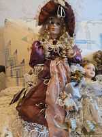 Front view of largest burgundy-dressed porcelain doll seated on sofa