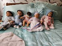 Five baby dolls arranged on bed showing overall lot