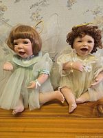 Front view of both dolls seated on wood surface