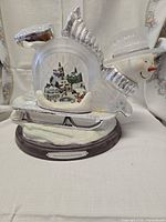 Full view of snow globe showing snowman, frosted globe, sleigh base, title plaque