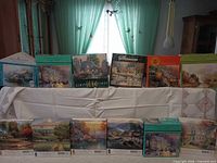 Front view of all twelve Thomas Kinkade puzzle boxes displayed in two rows