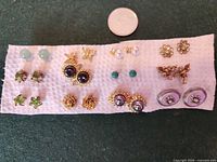Front view of all earring pairs on fabric strip with coin for scale