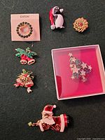 All seven brooches displayed including Eaton wreath on card, boxed Christmas tree, penguin, small wreath, two bell brooches, Santa sleigh