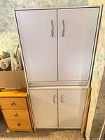 Two modular white laminate cabinets stacked, showing upper and lower double-door sections