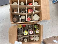 Two cardboard boxes containing roughly 30 vintage glass jars with assorted metal lids