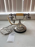 Front view of chrome rotary desk telephone with handset, cords, dial, base
