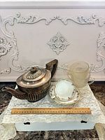 Group shot of teapot, cup & saucer, two glass creamers with ruler for scale
