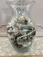 Flared clear glass vase filled with assorted costume jewelry pieces