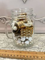 Jar showing assorted gold-tone jewelry and white beads with ruler for scale