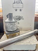 Group shot of ceramic jug on stand beside aluminum tube, background board