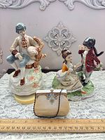 Group shot showing both porcelain figurines and minaudière with ruler for scale