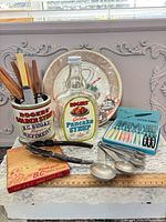 Group shot of all items including bottle, tin, knives, forks, spoons, nutcracker, apple slicer box