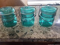 Front view of three teal Ball Ideal jars showing embossed eagle and wire bails