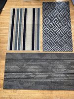 Front view of three mats: striped, grey geometric, charcoal runner
