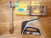 Stapler, two staple boxes and wrench laid out on wooden surface