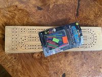wooden cribbage board and sealed peg pack displayed on wood surface
