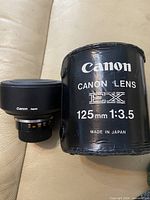Lens alongside branded hard case showing model and aperture