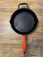 Top view of cast iron skillet showing interior, long handle with orange grip, helper handle, pour spouts